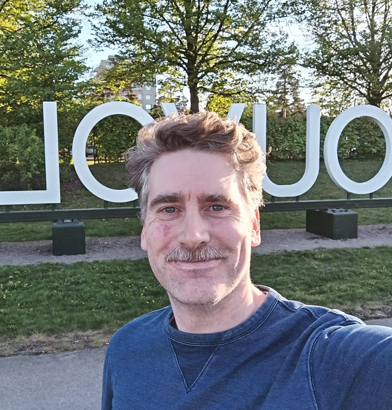Valokuva. Petteri Hyvärinen seisoo suurten Kouvola-kirjainten edessä ja katsoo kameraan.