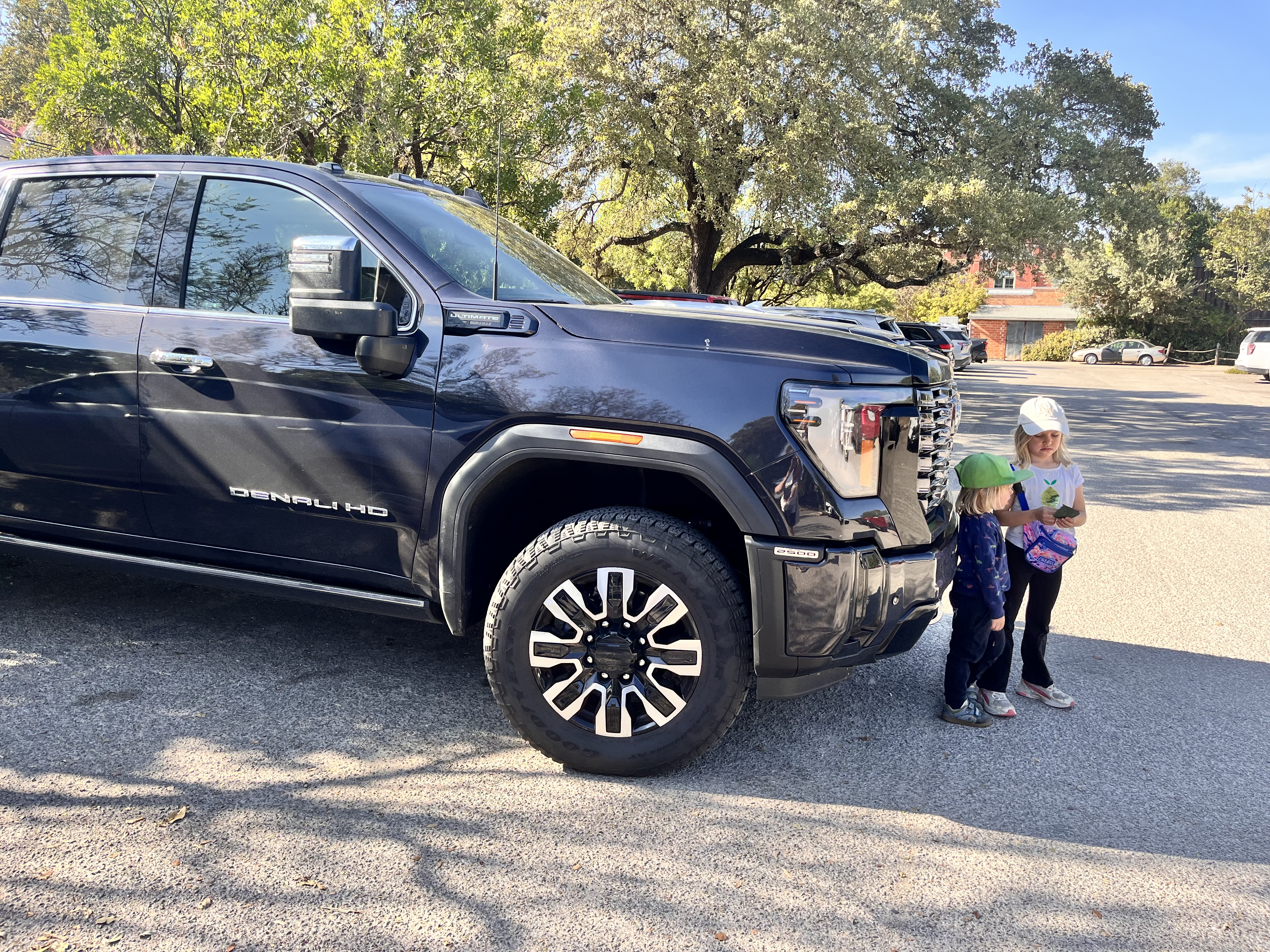 Valokuva isosta mustasta citymaasturista, jonka etuosa on korkeampi kuin kumpikaan kuvan lapsista, jotka seisovat ihan auton edessä.