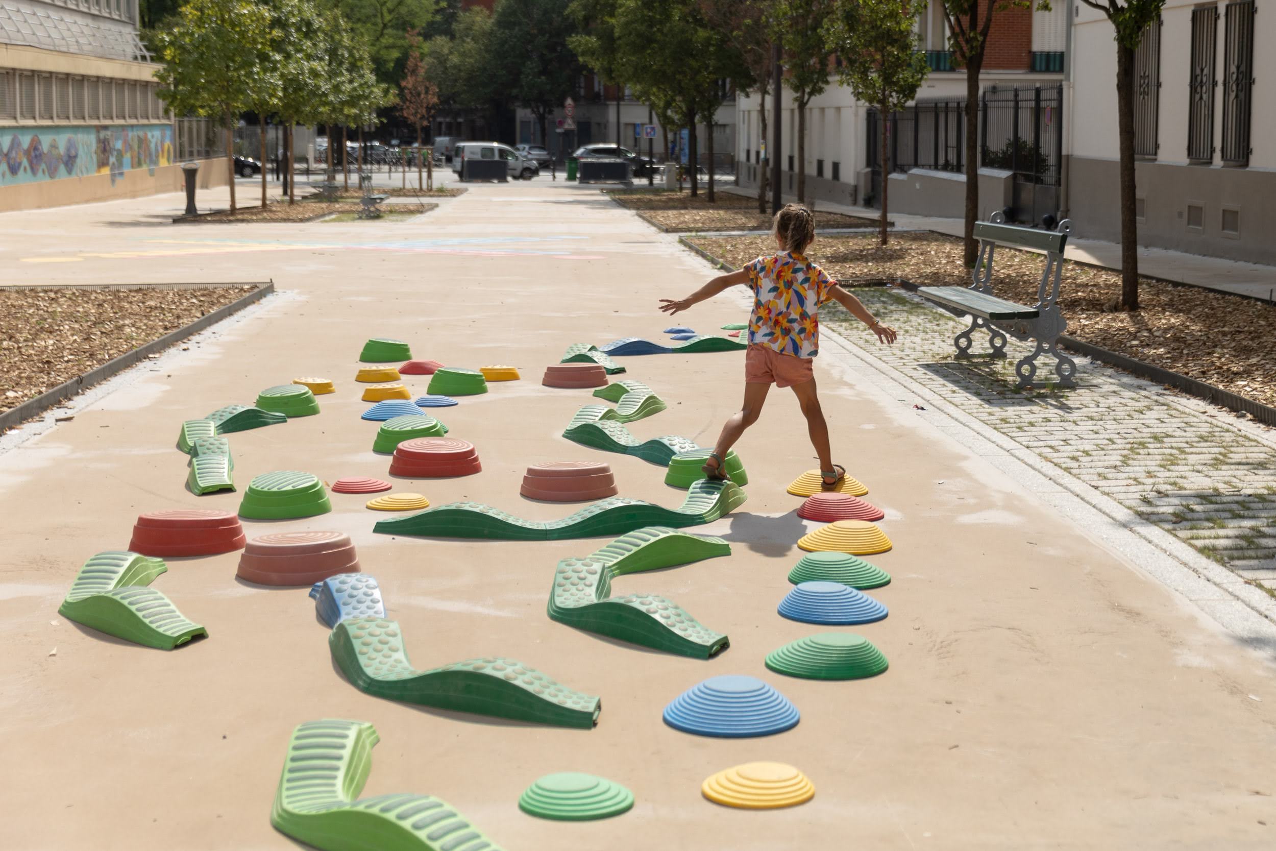 Valokuva kesäisestä kadusta, jolle on rakennettu pieni kohoesterata, jonka päällä lapsi hyppii.